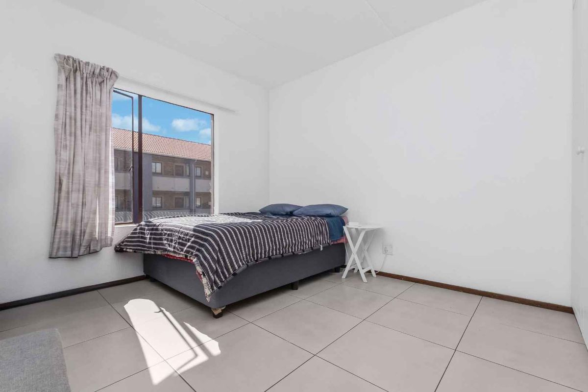 A simple bedroom featuring neutral tiled flooring and a large window providing natural light.