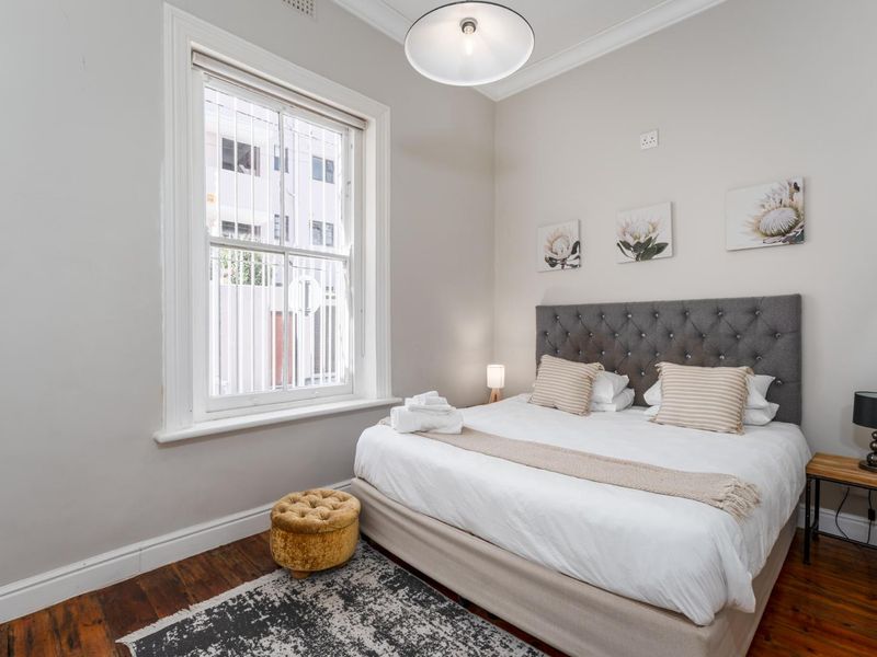 A well-maintained bedroom featuring classic timber flooring, decorative cornice, and a large sash window providing natural light.