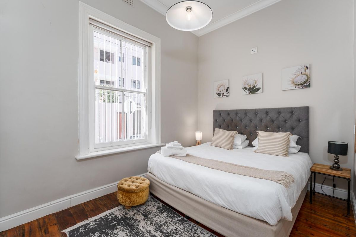 A well-maintained bedroom featuring classic timber flooring, decorative cornice, and a large sash window providing natural light.