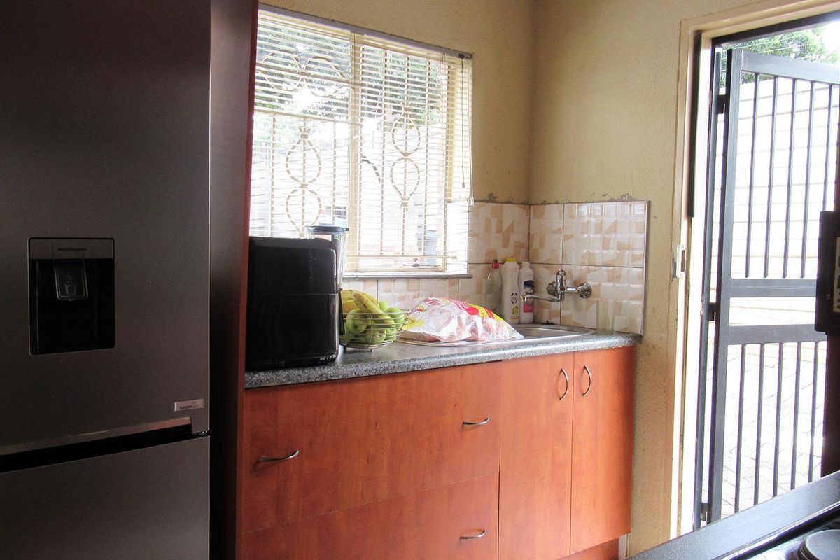 A compact kitchen area featuring wooden cabinetry, a granite-look countertop, a single sink, and direct access to an exterior door.