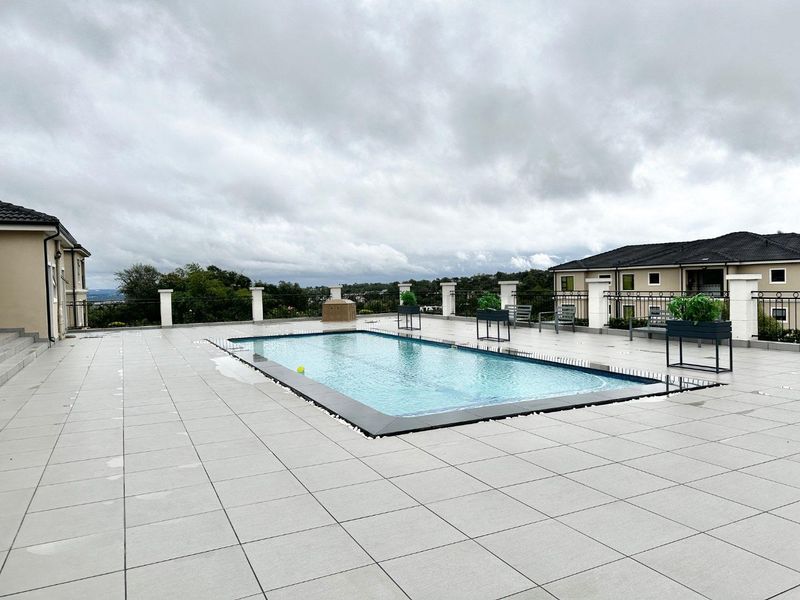 A spacious outdoor pool area featuring a rectangular swimming pool, large format tiled decking, and metal balustrades with scenic views.