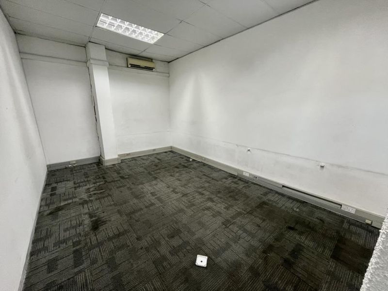 An empty industrial office space featuring carpeted flooring, a suspended ceiling with recessed lighting, and a wall-mounted air conditioning unit.