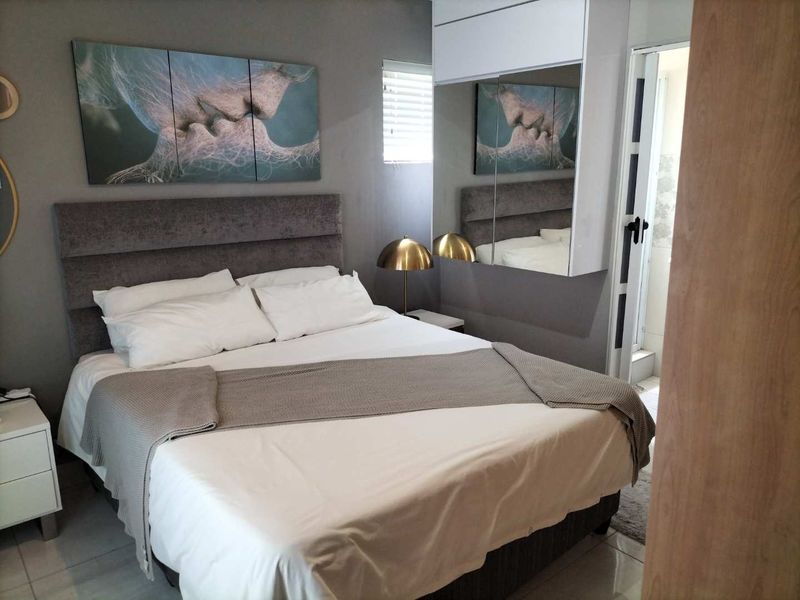 A well-maintained bedroom featuring built-in cupboards with mirrored doors, tiled flooring, and neutral wall finishes.