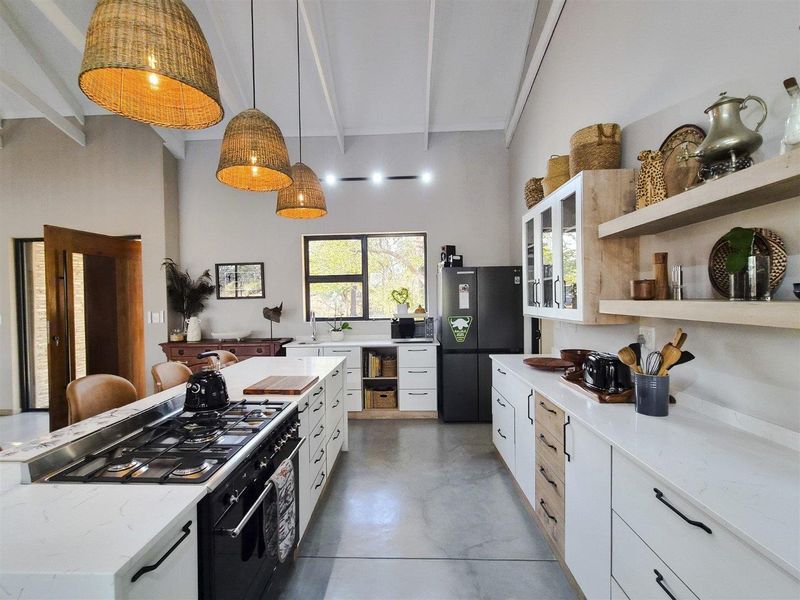 Modern kitchen featuring a large island with gas hob, quartz countertops, polished concrete floors, and exposed beam ceilings with stylish pendant lighting.