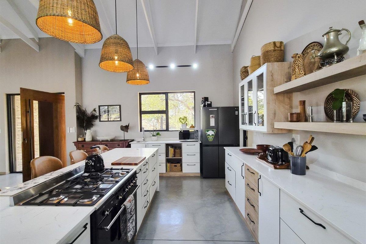 Modern kitchen featuring a large island with gas hob, quartz countertops, polished concrete floors, and exposed beam ceilings with stylish pendant lighting.