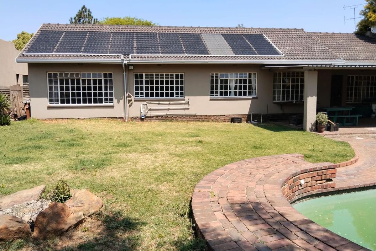 Rear view of the house featuring a tiled roof with solar panels, grid-style windows, a paved pool surround, and a garden area.