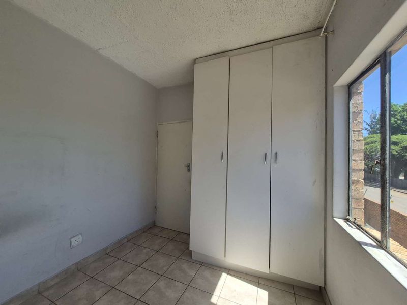 A vacant bedroom featuring tiled flooring, a built-in wardrobe, and a window providing natural light.