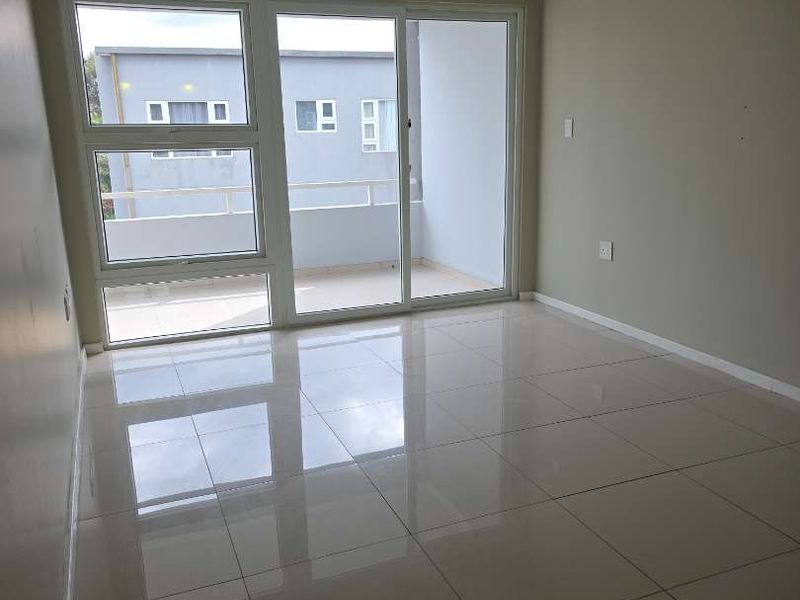 A bright, empty living room featuring polished tile flooring, recessed lighting, and a large sliding glass door providing access to an outdoor balcony.
