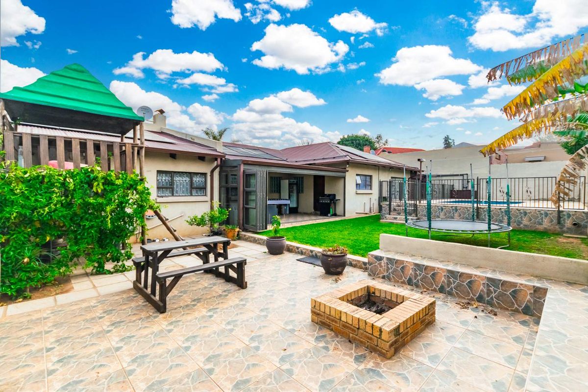 Spacious rear garden featuring a paved patio area with a built-in brick fire pit, lawn, and access to a covered outdoor entertainment space.