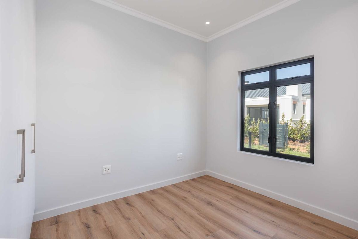 A bright, modern bedroom featuring light wood-look flooring, built-in cabinetry, and a large window with dark frames.