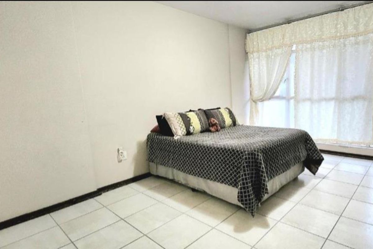 A bedroom featuring tiled flooring and large windows with curtains, providing natural light and a simple, functional layout.