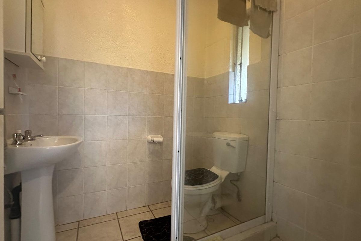 A functional bathroom featuring a pedestal basin, a toilet, and a glass-enclosed shower area with tiled walls and flooring.