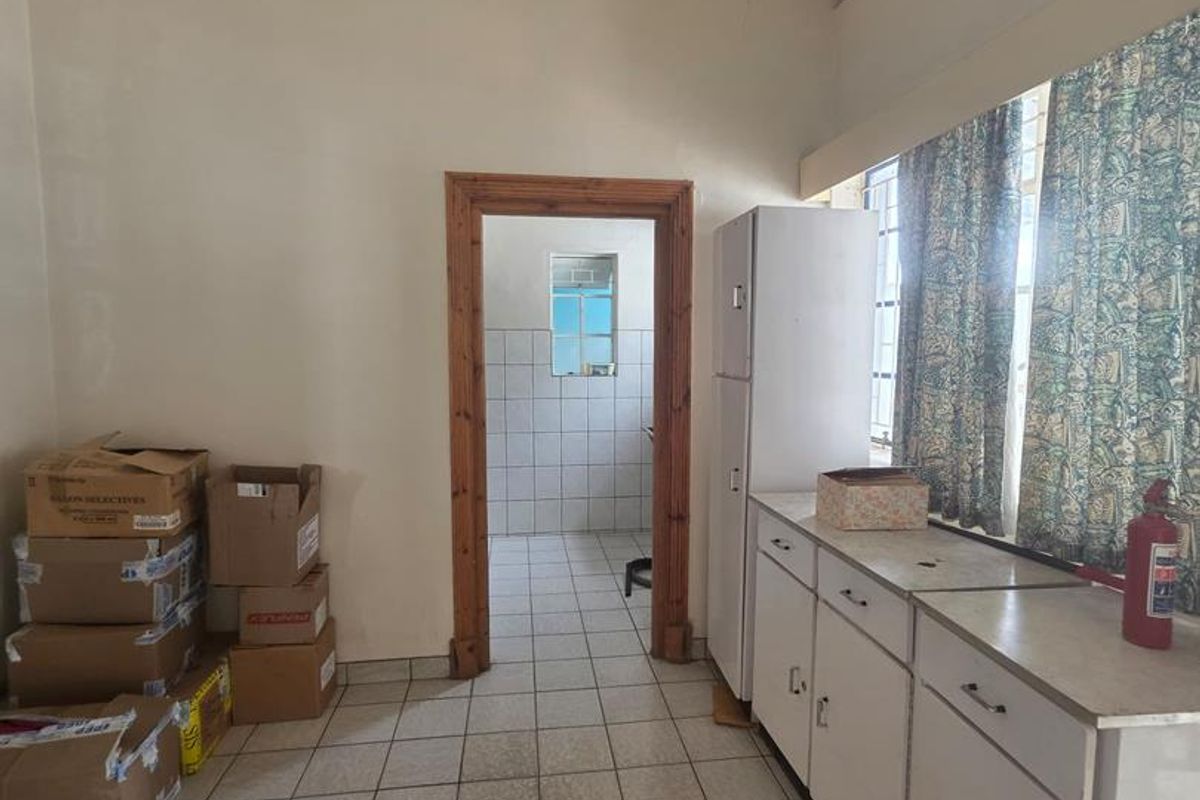 A functional kitchen area featuring built-in white cabinetry, tiled flooring, and a doorway leading to an adjacent utility space.