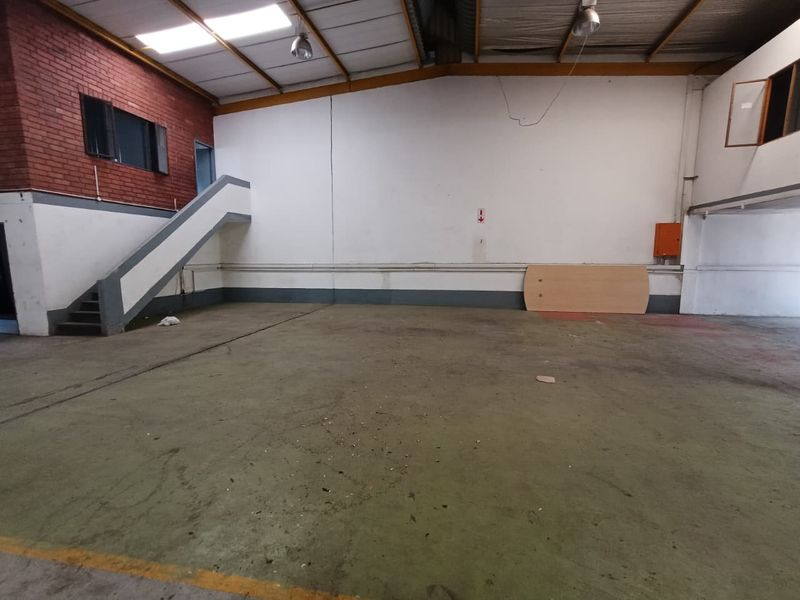 Spacious industrial warehouse unit featuring high ceilings, exposed steel roof structure, concrete flooring, and an internal staircase leading to an upper level.