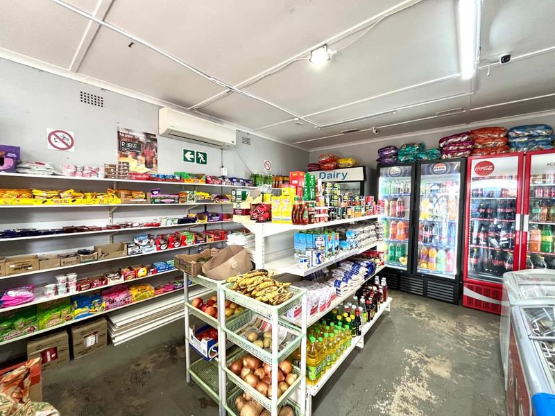 Interior view of a retail convenience store featuring fixed shelving, commercial refrigeration units, and wall-mounted air conditioning.