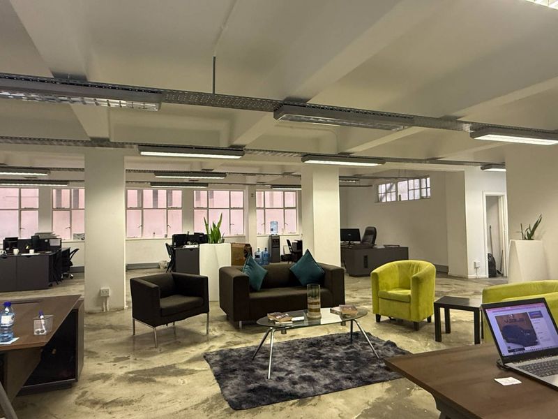 Spacious open-plan office featuring industrial-style exposed ceilings, polished concrete floors, and large windows providing ample natural light.