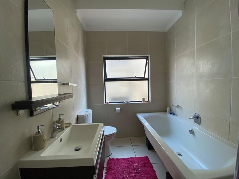 A functional bathroom featuring a vanity with basin, a bathtub, and neutral wall tiling, providing a clean and practical space.