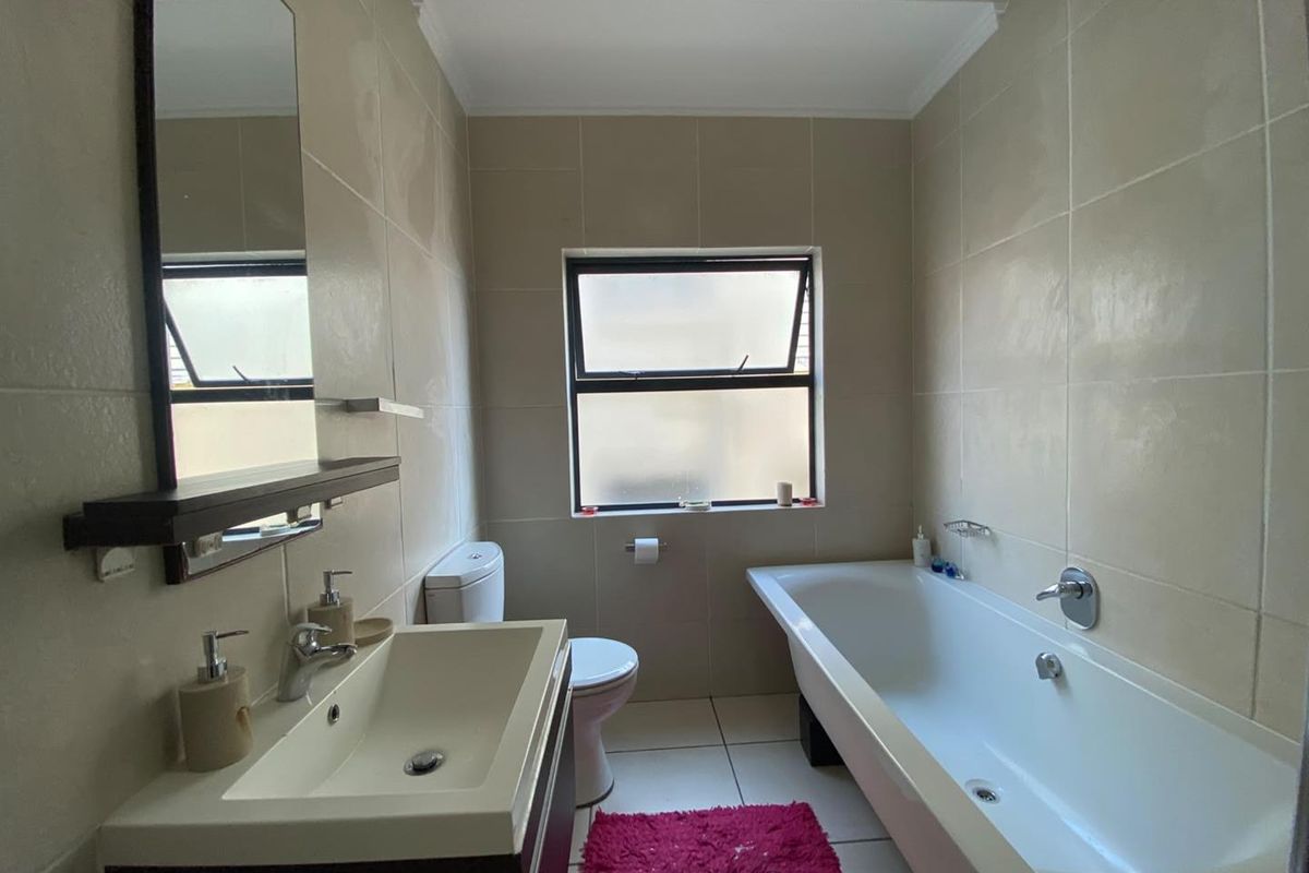 A functional bathroom featuring a vanity with basin, a bathtub, and neutral wall tiling, providing a clean and practical space.