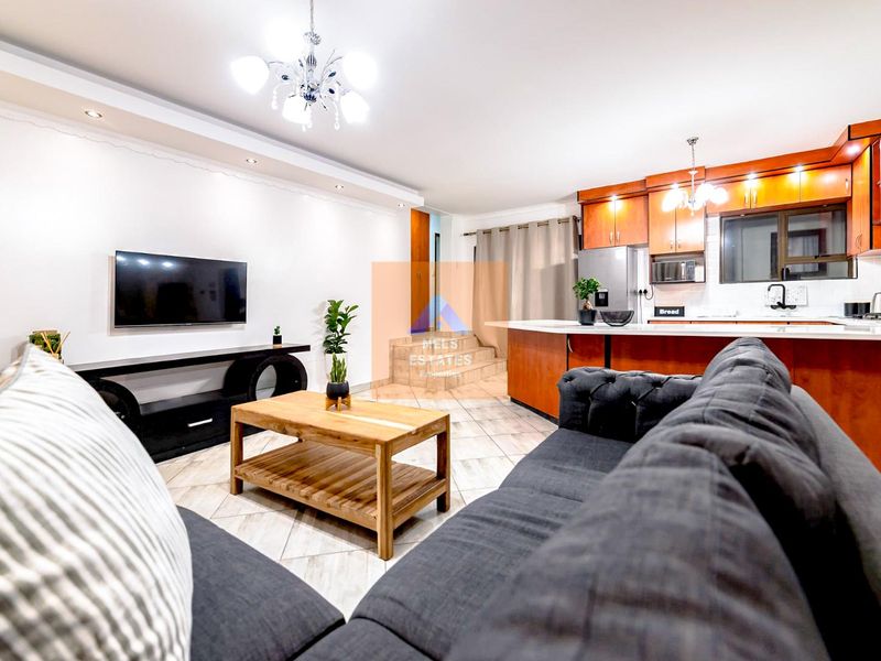 An open-plan living and kitchen area featuring tiled floors, modern cabinetry, and recessed lighting, creating a functional and cohesive living space.