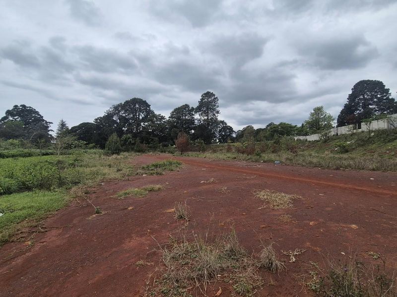 A view of a vacant commercial land plot featuring cleared earth and a precast concrete boundary wall along the perimeter.