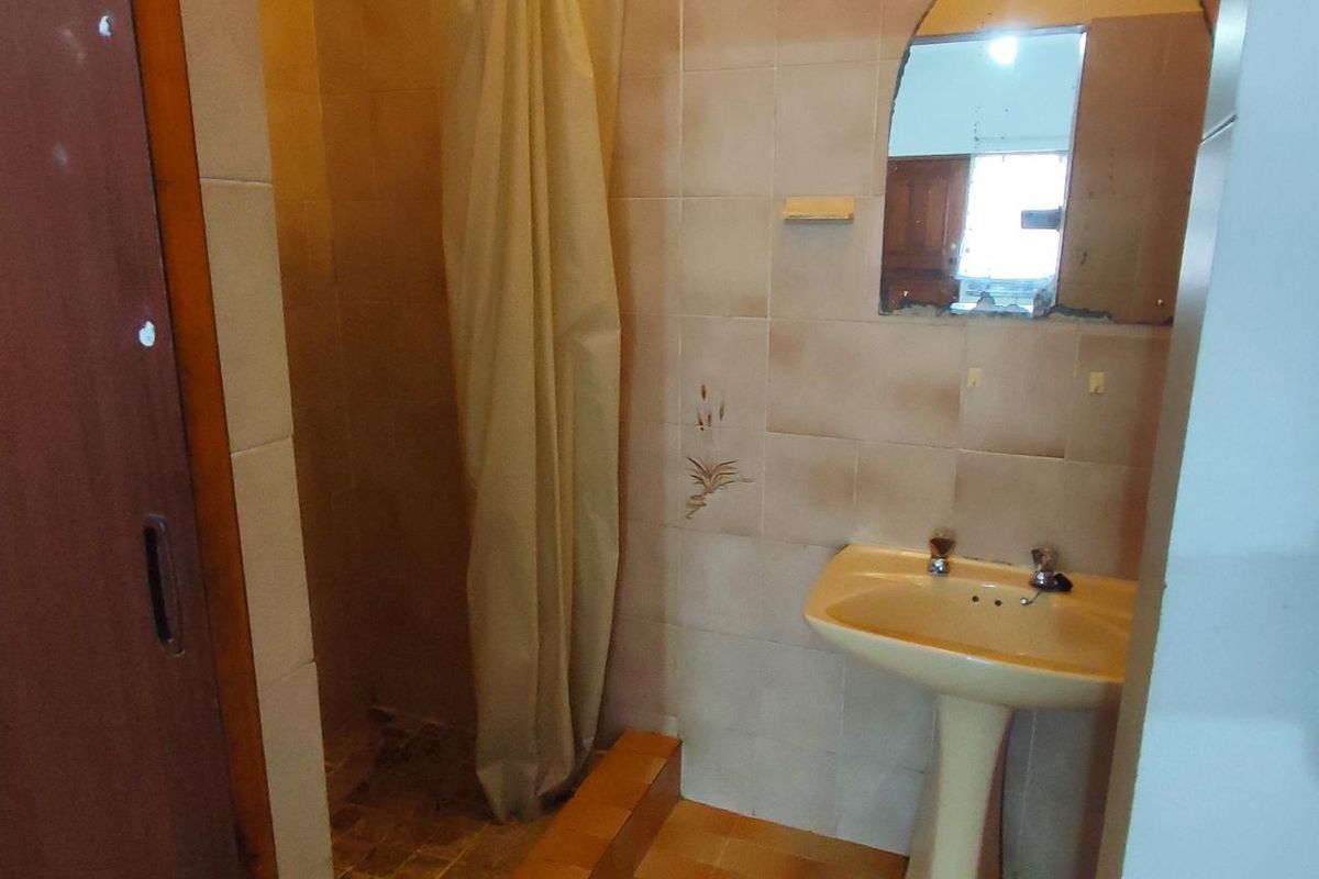 A dated bathroom featuring a pedestal basin and a shower enclosure with tiled walls and flooring, requiring modernization and cosmetic updates.