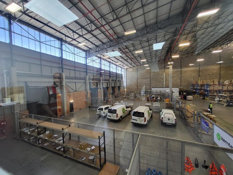 Spacious industrial warehouse facility featuring high ceilings, exposed steel trusses, concrete flooring, and integrated office or mezzanine viewing area.