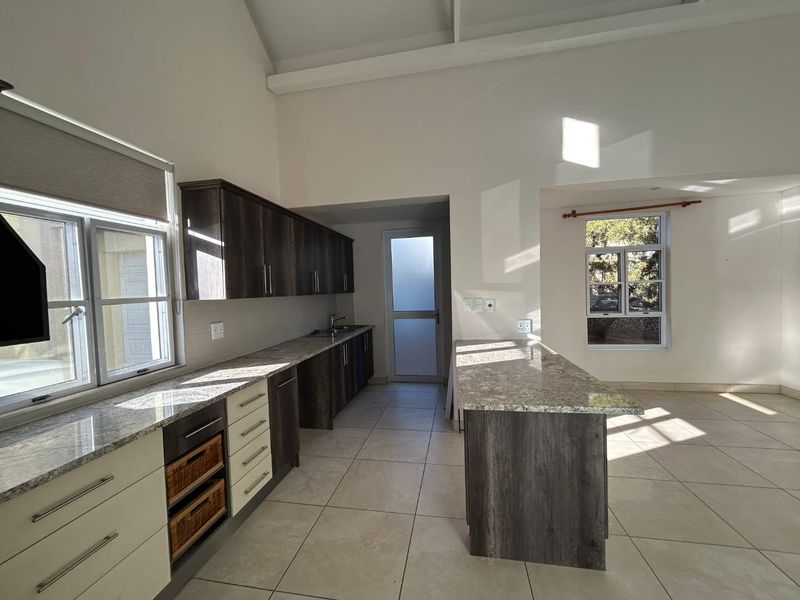 Spacious open-plan kitchen featuring granite countertops, ample built-in cabinetry, a central island, and tiled flooring under a high vaulted ceiling.