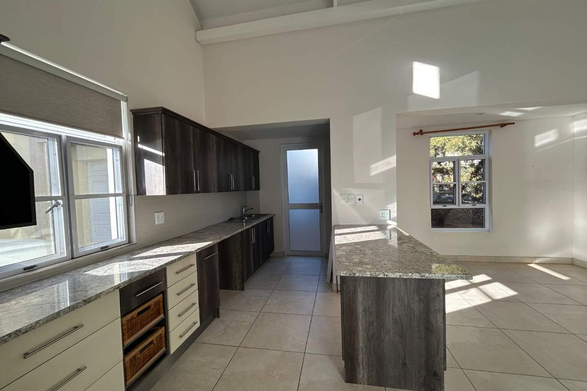 Spacious open-plan kitchen featuring granite countertops, ample built-in cabinetry, a central island, and tiled flooring under a high vaulted ceiling.