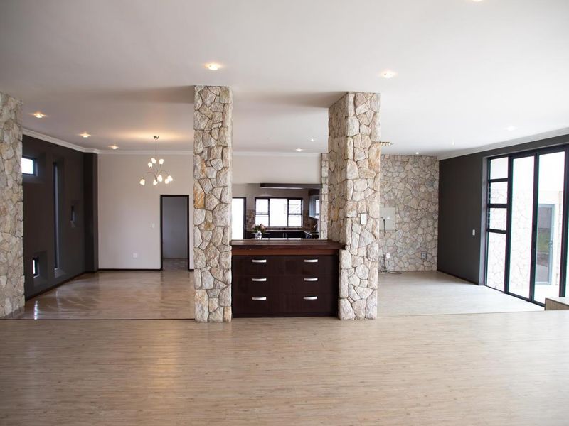 Spacious open-plan living area featuring striking stone-clad pillars, modern laminate flooring, and large aluminium sliding doors providing ample natural light.