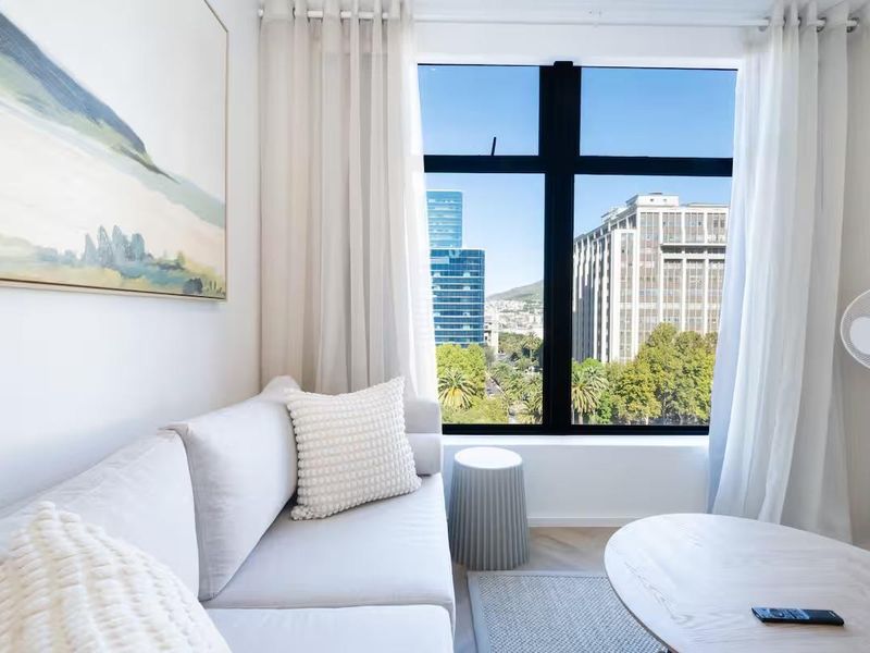 A bright living room featuring modern herringbone flooring and a large window offering expansive city views.