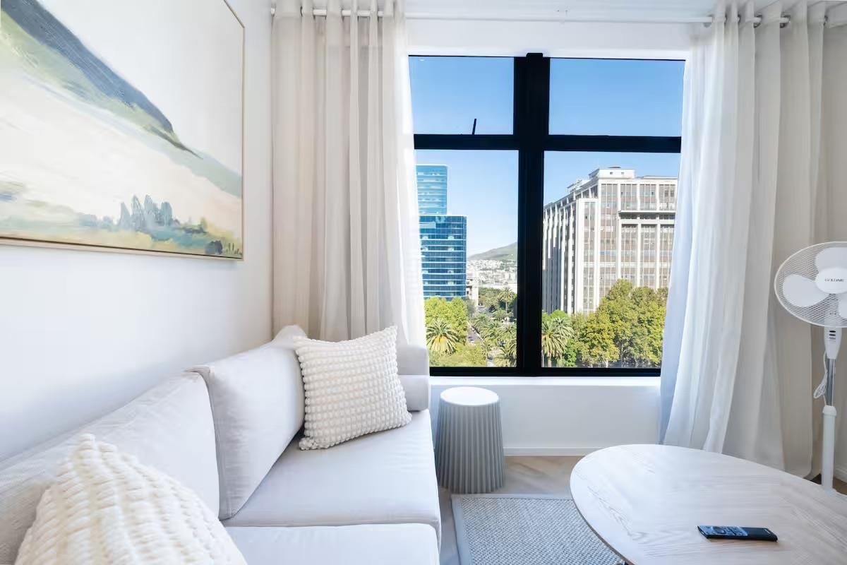 A bright living room featuring modern herringbone flooring and a large window offering expansive city views.
