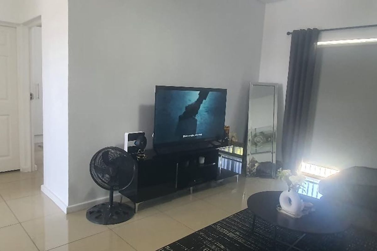 A living room featuring neutral tiled flooring and a clean, minimalist layout with access to adjacent rooms.