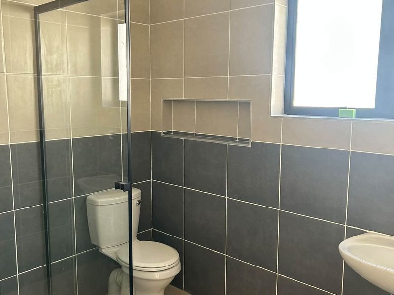 A modern bathroom featuring a glass shower enclosure, wall-mounted basin, toilet, and neutral-toned tiled walls with a convenient recessed storage niche.