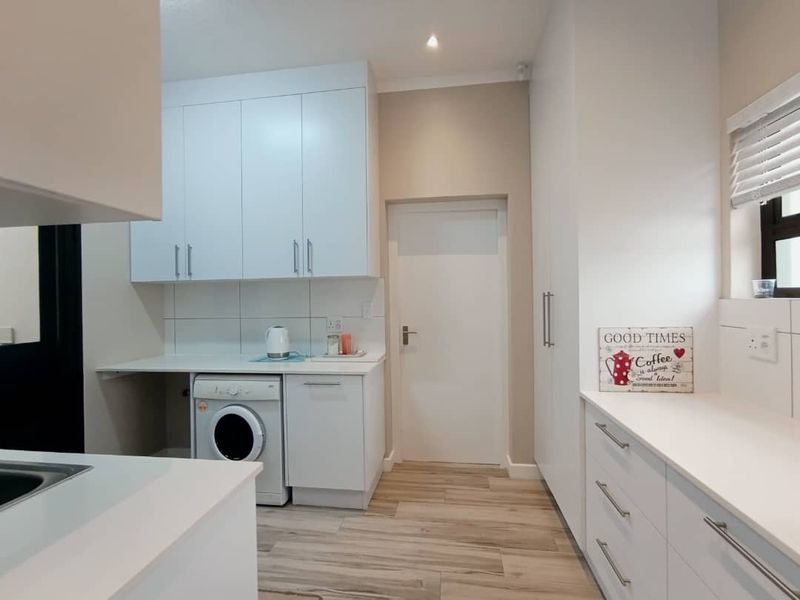 A clean and modern laundry room featuring white built-in cabinetry, ample counter space, and light wood-look laminate flooring.