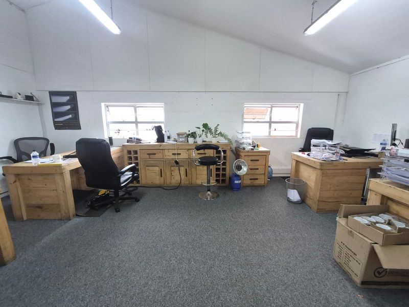 A functional industrial office space featuring carpeted flooring, pitched ceilings, and natural light from casement windows.