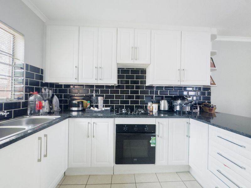 A well-maintained kitchen featuring white cabinetry, contrasting black subway tile backsplash, granite countertops, and integrated appliances including a gas hob and oven.