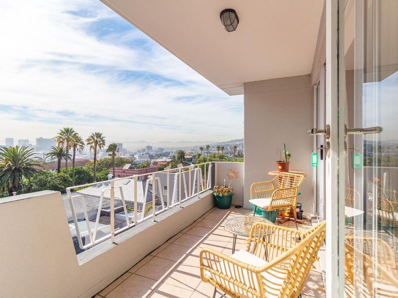 A spacious covered balcony featuring tiled flooring, a metal balustrade, and expansive elevated views of the surrounding cityscape.
