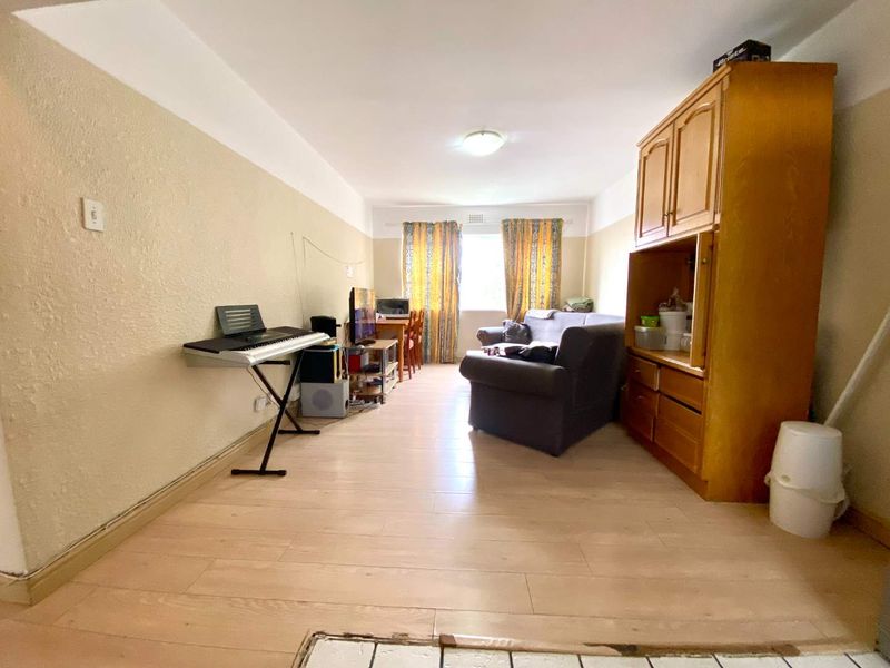 A living room area featuring laminate flooring and neutral wall finishes, offering a functional space with potential for modernization and aesthetic updates.