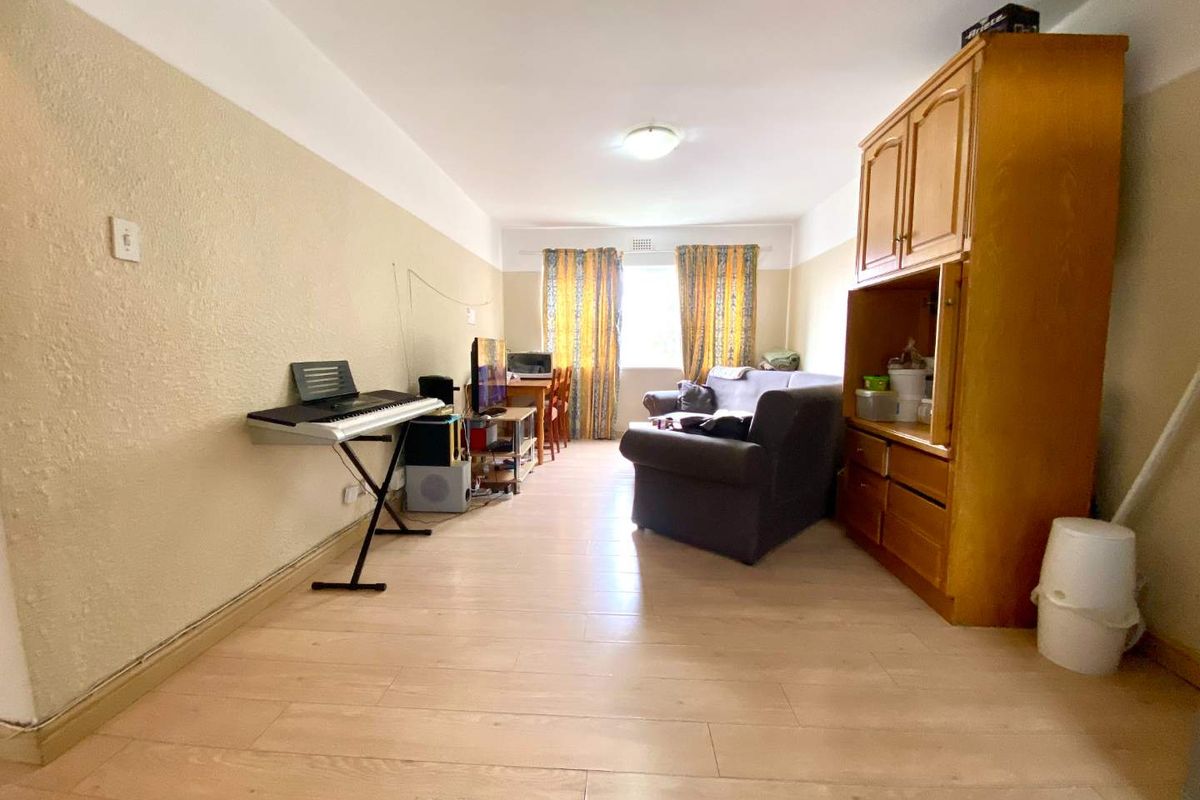 A living room area featuring laminate flooring and neutral wall finishes, offering a functional space with potential for modernization and aesthetic updates.