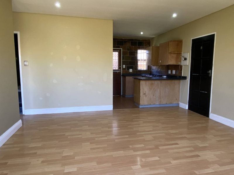 Open-plan living area featuring laminate flooring and recessed lighting, flowing into a functional kitchen with built-in cabinetry and stone countertops.