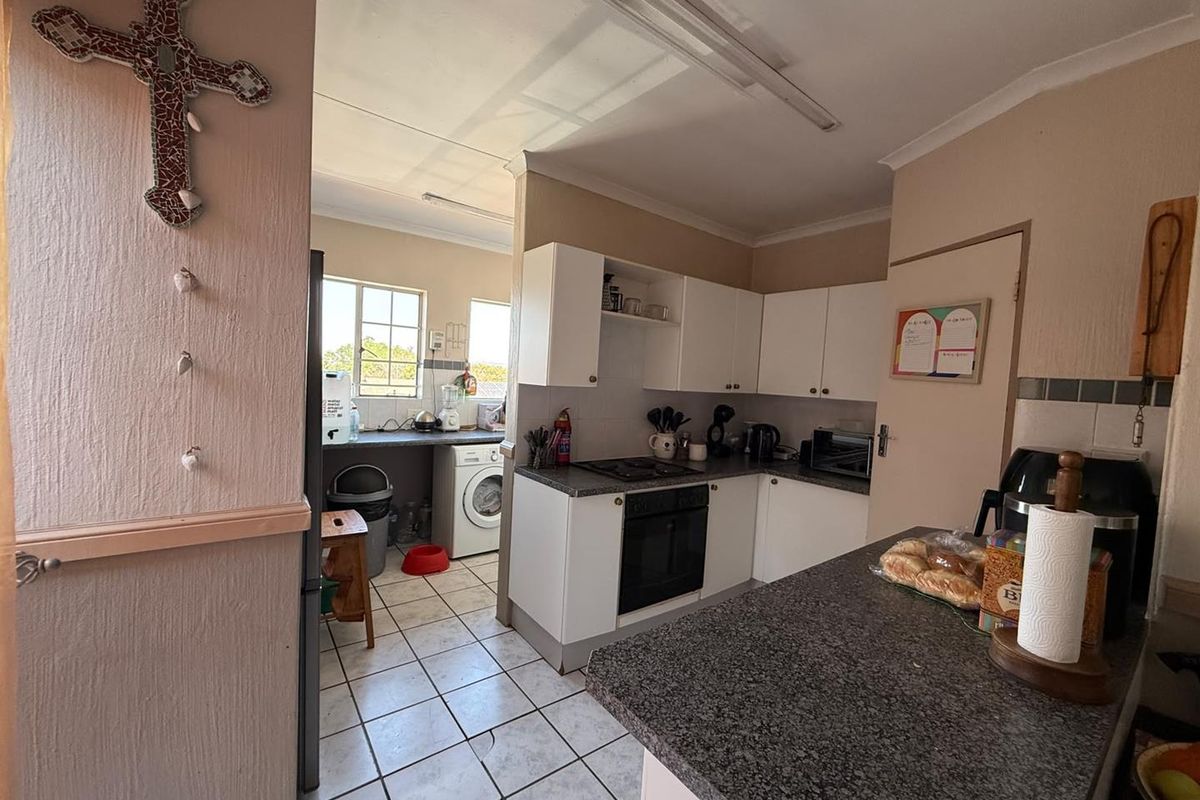 Functional kitchen featuring white cabinetry, granite countertops, built-in oven and hob, with an adjoining scullery area and tiled flooring throughout.