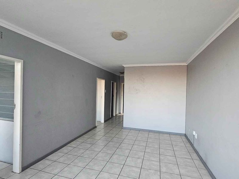 An empty living area featuring neutral tiled flooring, grey painted walls, and ceiling cornice detailing, ready for personalization.