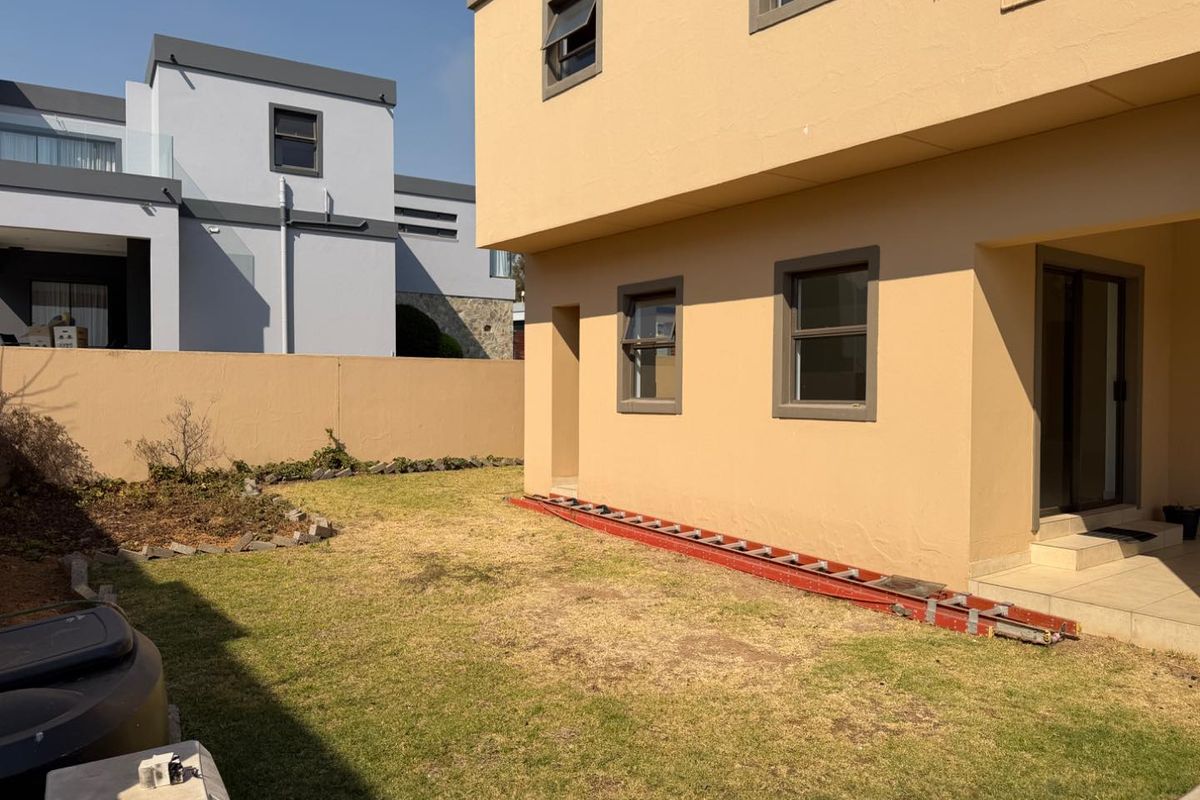 Rear exterior view of the property featuring a small lawn, boundary wall, and tiled patio area with access to the main dwelling.
