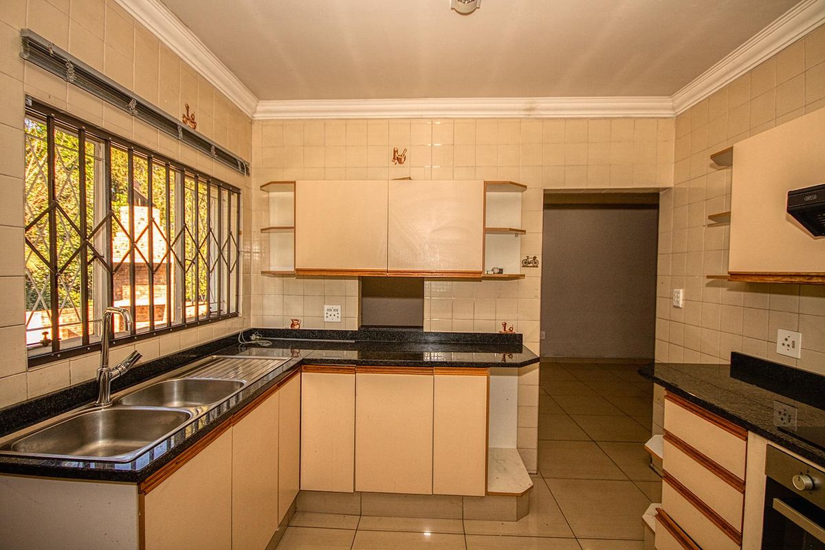 A dated kitchen featuring granite countertops, a double stainless steel sink, built-in oven, and tiled walls, requiring cosmetic updates to modernize the space.