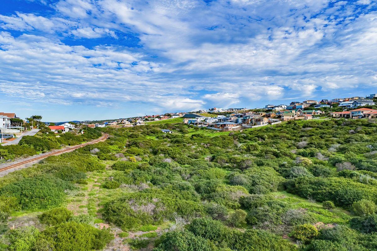 An aerial view of a vacant residential plot featuring native coastal vegetation and an adjacent railway line, set within a developed coastal neighborhood.