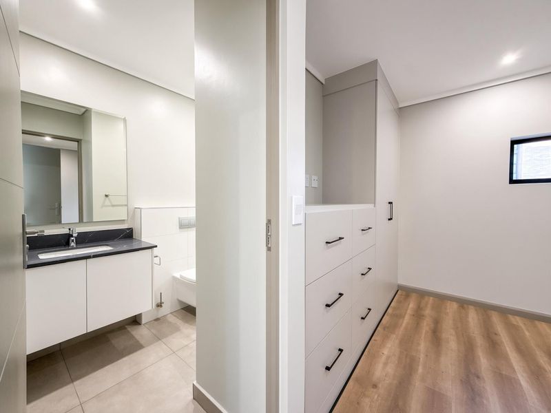 A modern bedroom featuring built-in storage cabinetry and an en-suite bathroom with a sleek vanity and wall-mounted toilet.