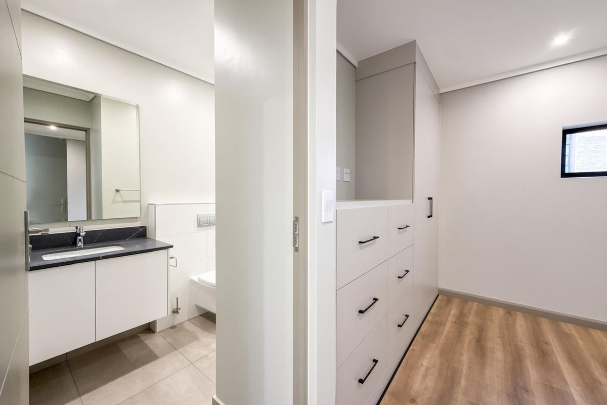 A modern bedroom featuring built-in storage cabinetry and an en-suite bathroom with a sleek vanity and wall-mounted toilet.