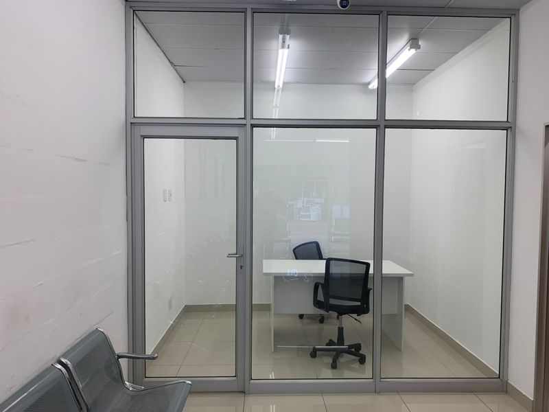 A modern, partitioned office space featuring aluminium-framed glass walls, tiled flooring, and integrated fluorescent lighting, providing a clean and professional work environment.