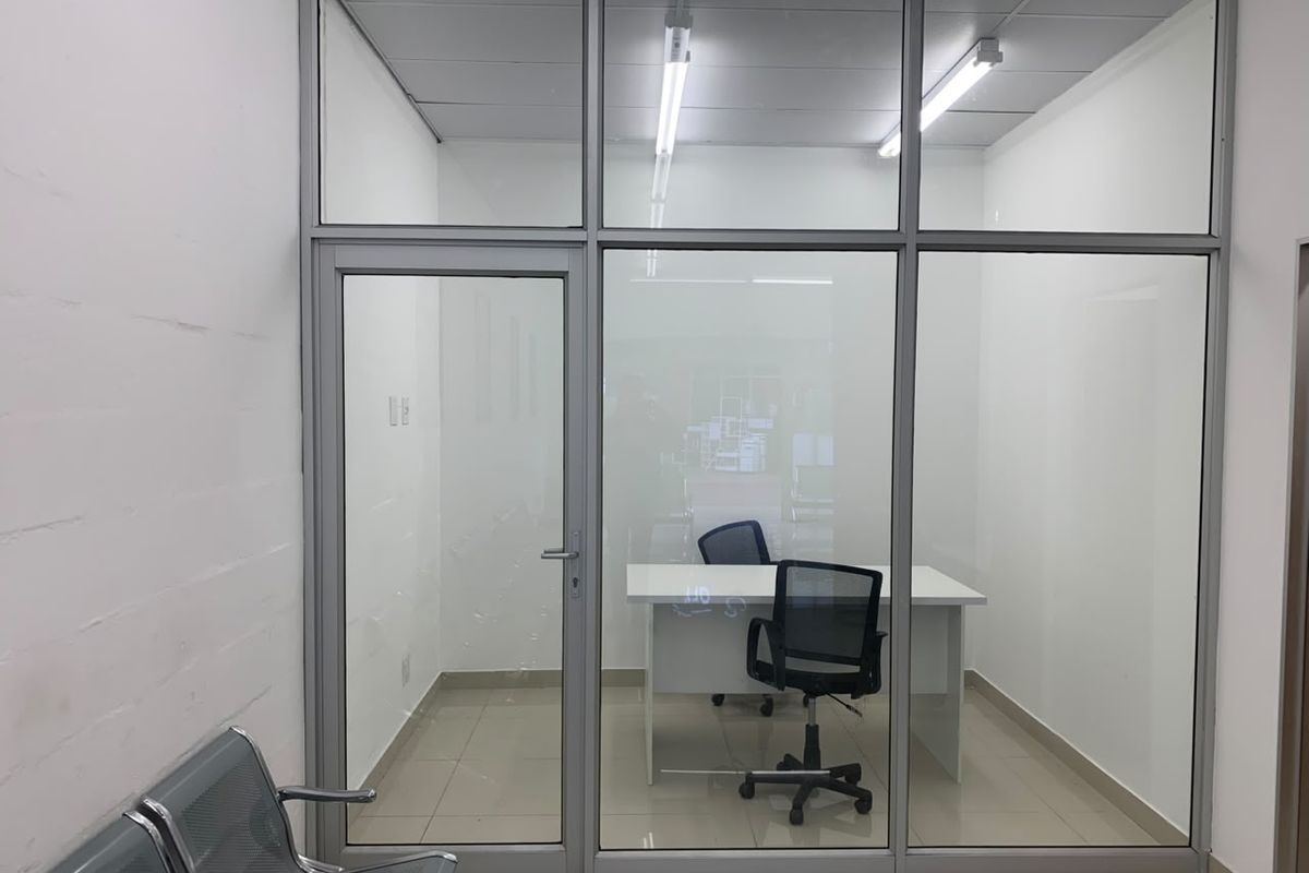 A modern, partitioned office space featuring aluminium-framed glass walls, tiled flooring, and integrated fluorescent lighting, providing a clean and professional work environment.