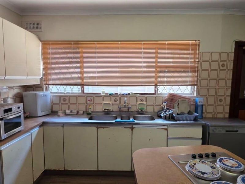 A dated kitchen featuring laminate cabinetry, a double sink, and a central island with a built-in hob, offering significant potential for modernization.